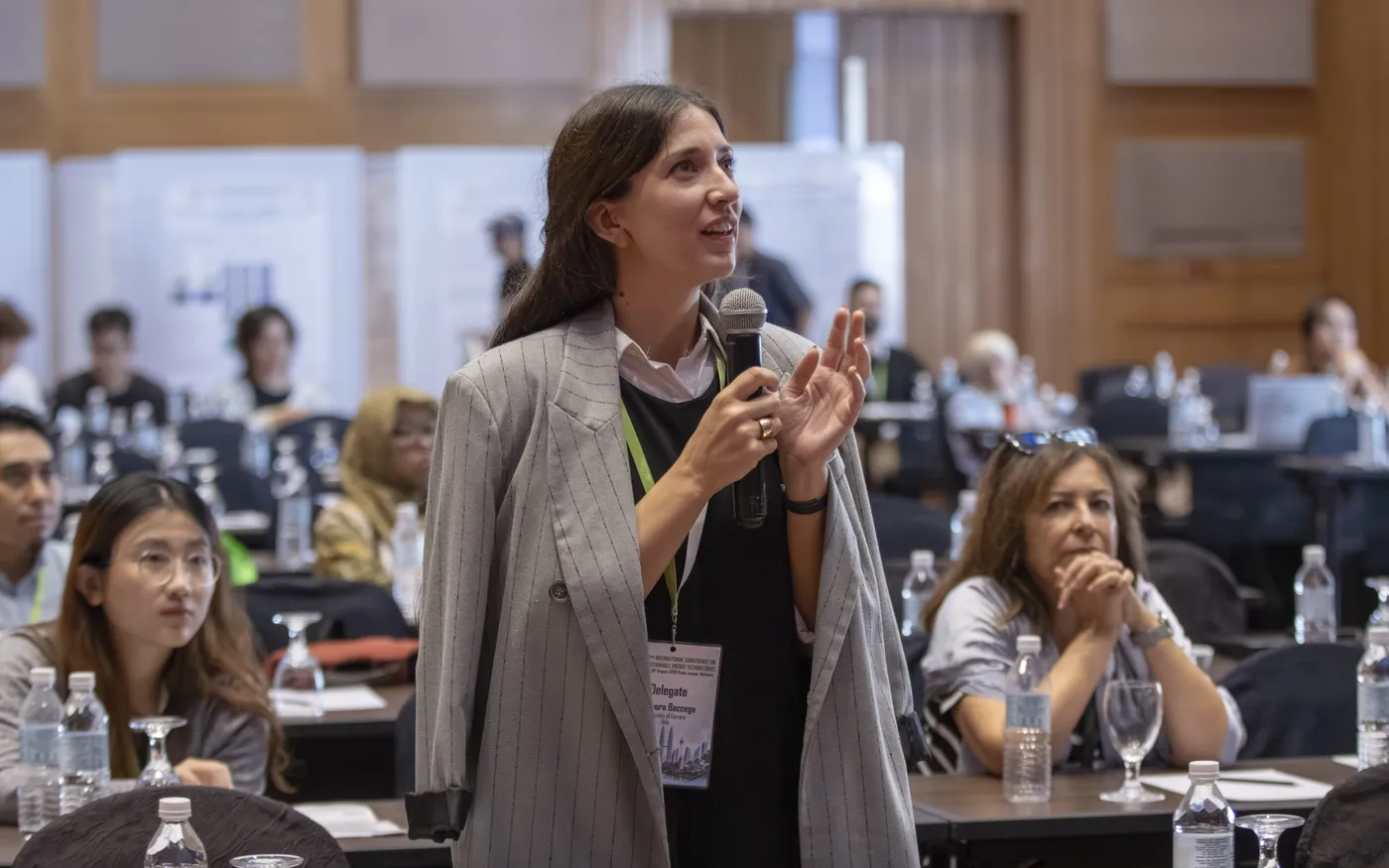 A delegate standing with a hand microphone to put a question to a session, with seated delegates listening.