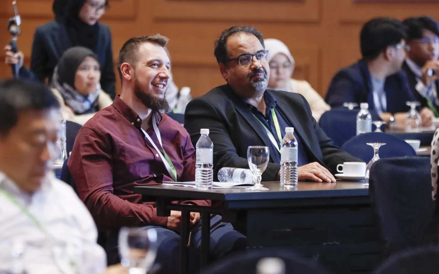 A row of delegates seated at a session table, listening and smiling.